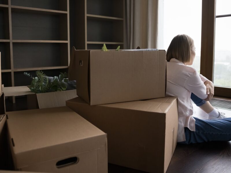 Woman experiencing homebuyers remorse after moving into new house sitting amidst moving boxes wondering if you can sell a house you just bought