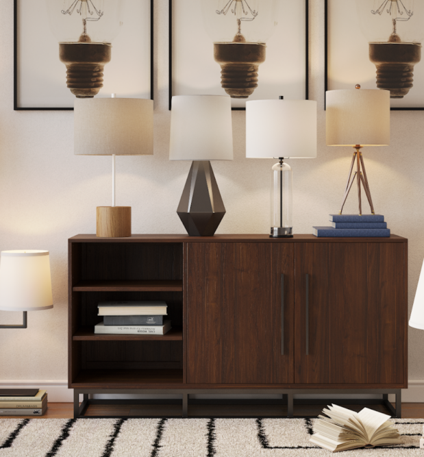 Side table in stylish neutral living room with different accent light table lamps from CORT Furniture Outlet across the surface, a stylish patterned rug, faux plants, and modern wall art ideas depicting light bulbs.